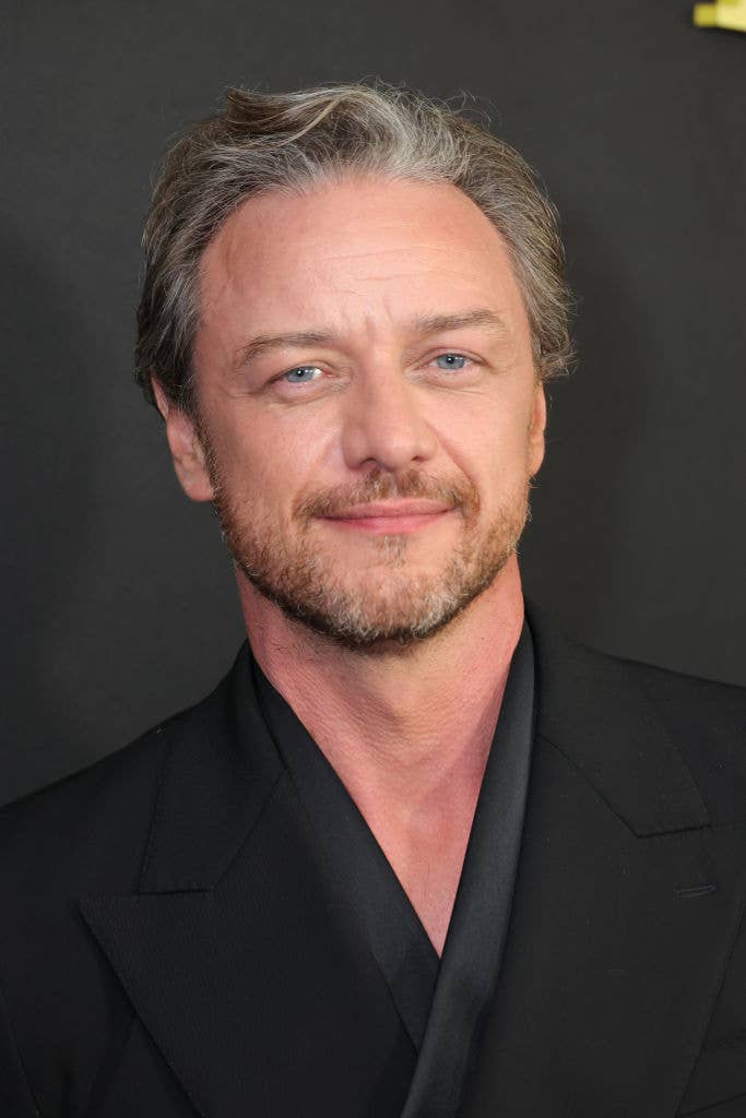 James McAvoy, dressed in a smart, black suit, is smiling on a red carpet