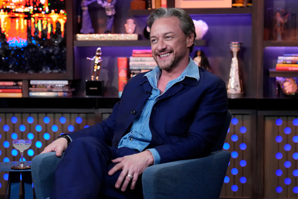 James McAvoy smiles while seated on a talk show set, dressed in a blue suit with a light blue shirt