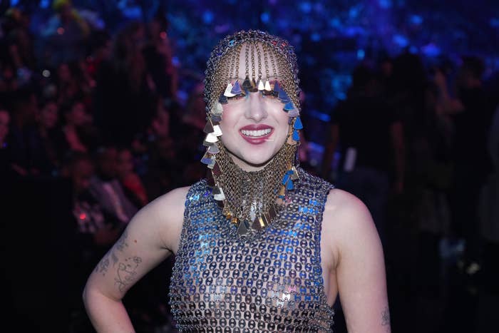 Person smiling, wearing a beaded mesh headpiece and matching outfit, on a red carpet or event setting