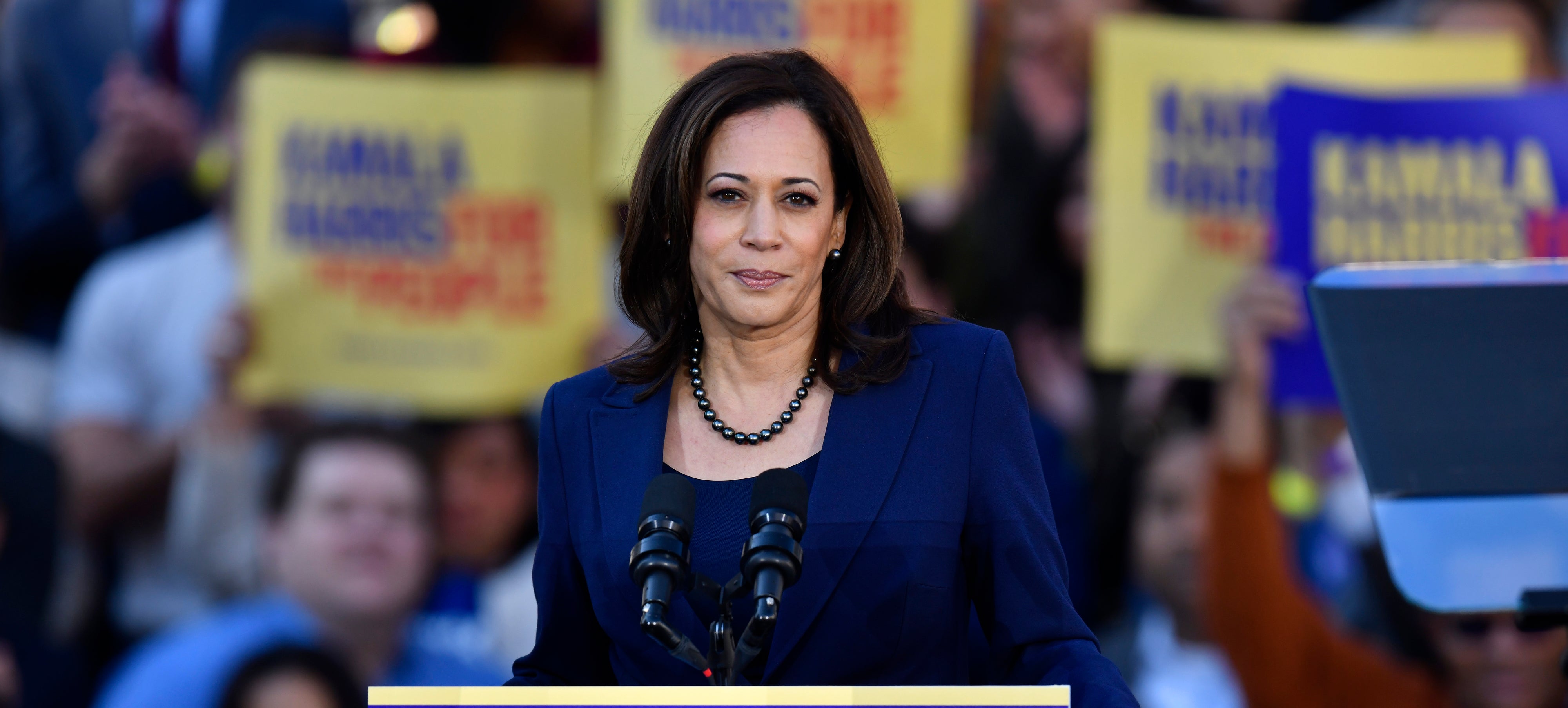 Kamala Harris speaking at an outdoor campaign event, standing behind a podium