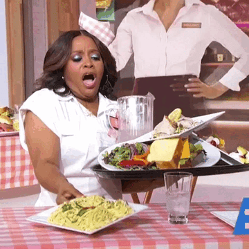 Sherri Shepherd, in a white outfit, reacts with surprise as a tray of food topples over at a restaurant-themed set on a TV show