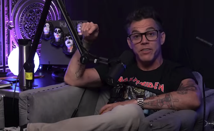 Steve-O, wearing an Iron Maiden t-shirt and glasses, sits in an armchair with a microphone nearby