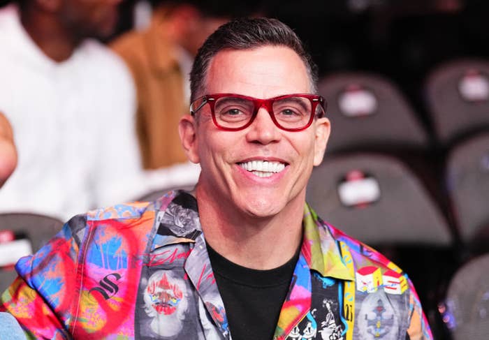 Steve-O smiles while wearing a vibrant, patterned shirt and red glasses at the event