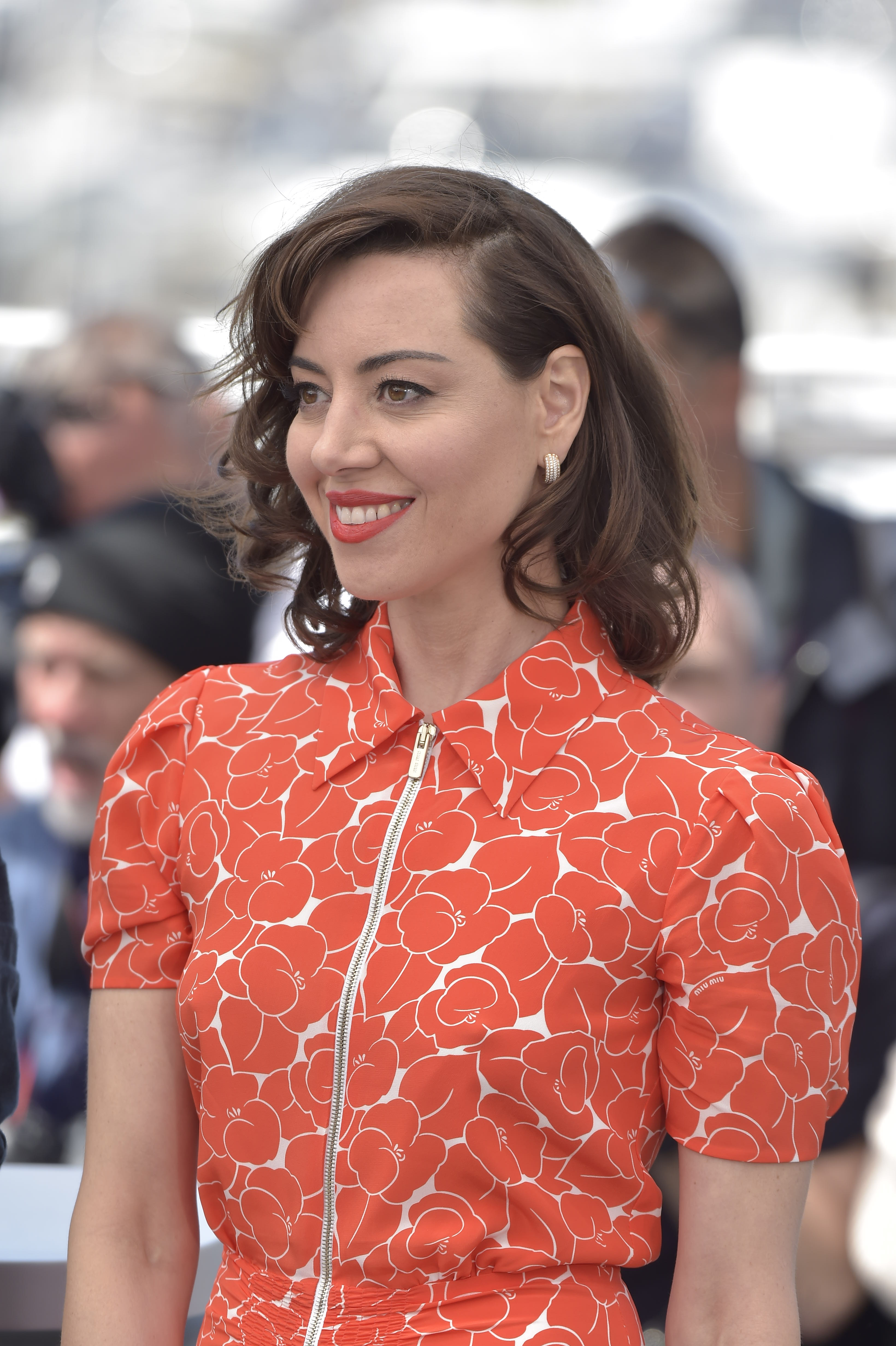 Aubrey Plaza is smiling at an event, wearing a stylish dress with a floral pattern and puffed sleeves