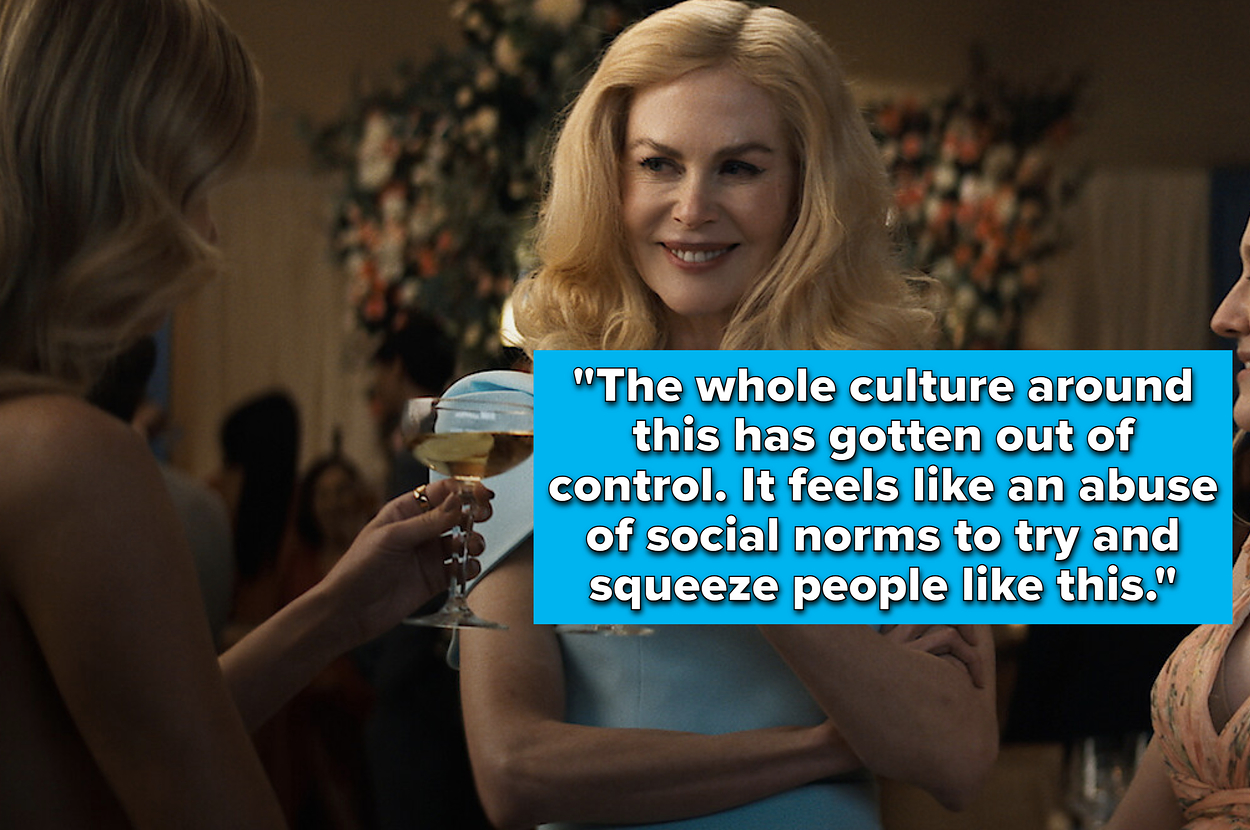 Nicole Kidman, in an elegant one-shoulder dress, smiles and holds a champagne glass while chatting with two women at a social event