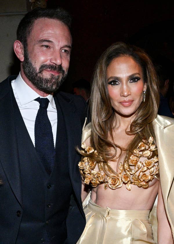 Ben Affleck and Jennifer Lopez posing together; Ben in a classic suit and tie, Jennifer in an embellished gown with floral accents