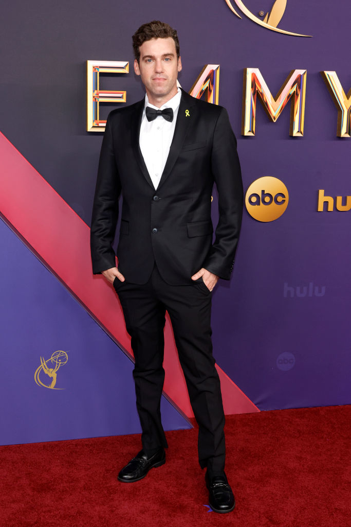 A man in a black tuxedo, white dress shirt, and black bow tie on the red carpet at the Emmy Awards