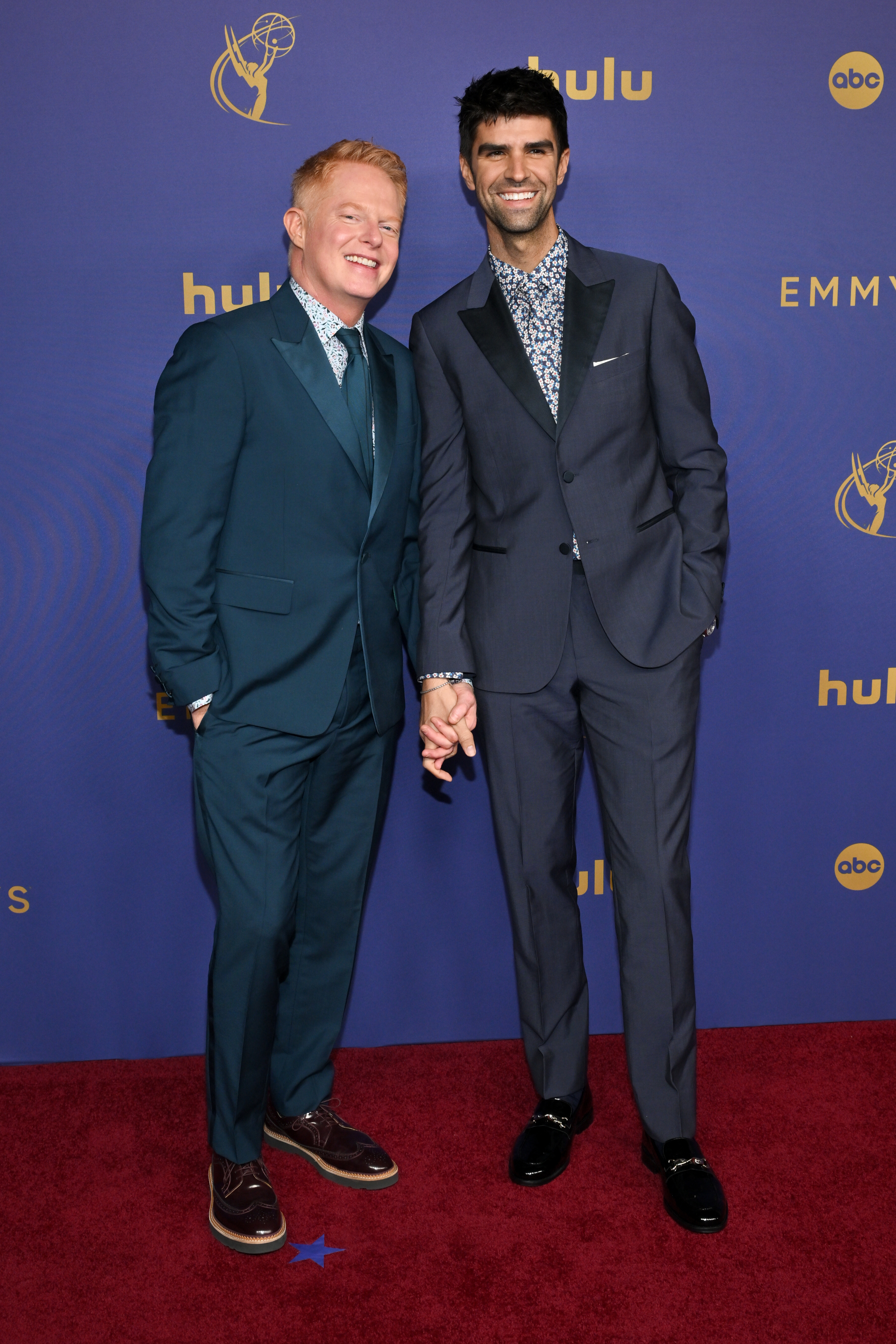 Jesse Tyler Ferguson and Justin Mikita on the red carpet at the Emmys, both in stylish suits, holding hands and smiling