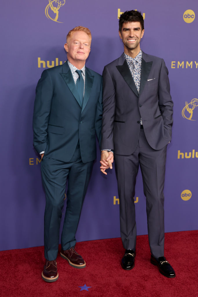 Jesse Tyler Ferguson and Justin Mikita, both in suits, holding hands on an event's red carpet