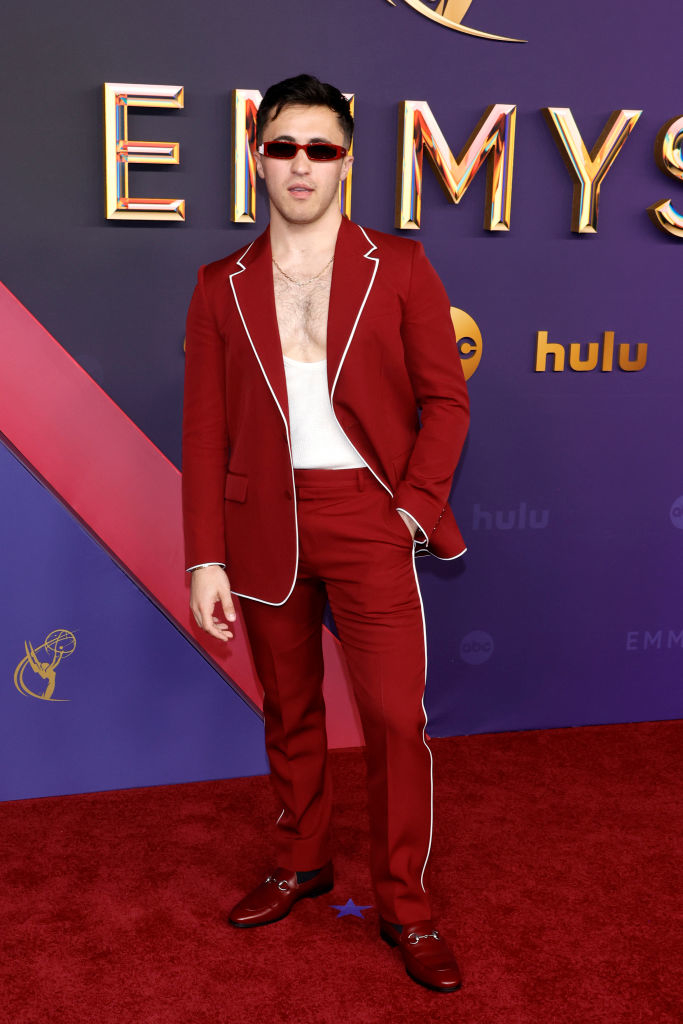 Man on red carpet at Emmys in red suit with white trim, white tank top, red sunglasses, and dress shoes