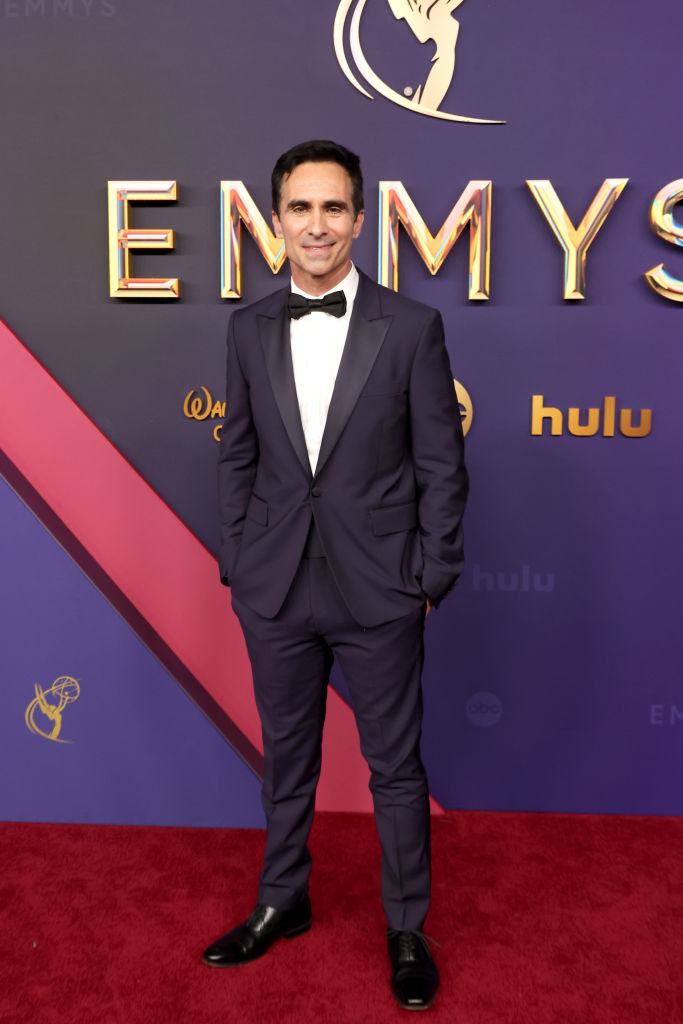 Nestor Carbonell at the Emmy Awards red carpet, dressed in a sleek black tuxedo with a bow tie, standing in front of the event's backdrop