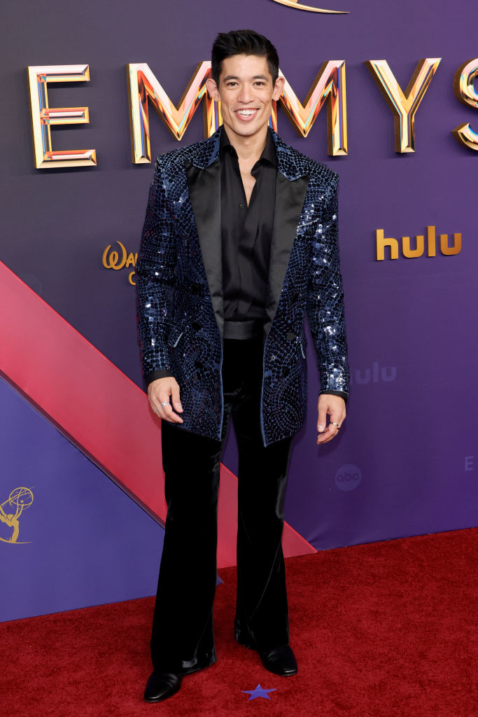 Actor Christopher Chung on the red carpet, wearing a sequined blazer, black shirt, and black pants, at the Emmy Awards