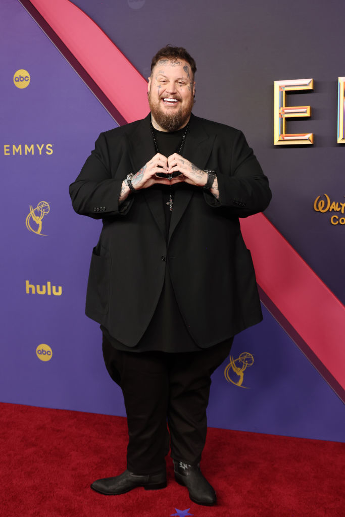 Smiling man with tattoos in all-black attire on the red carpet at the Emmys