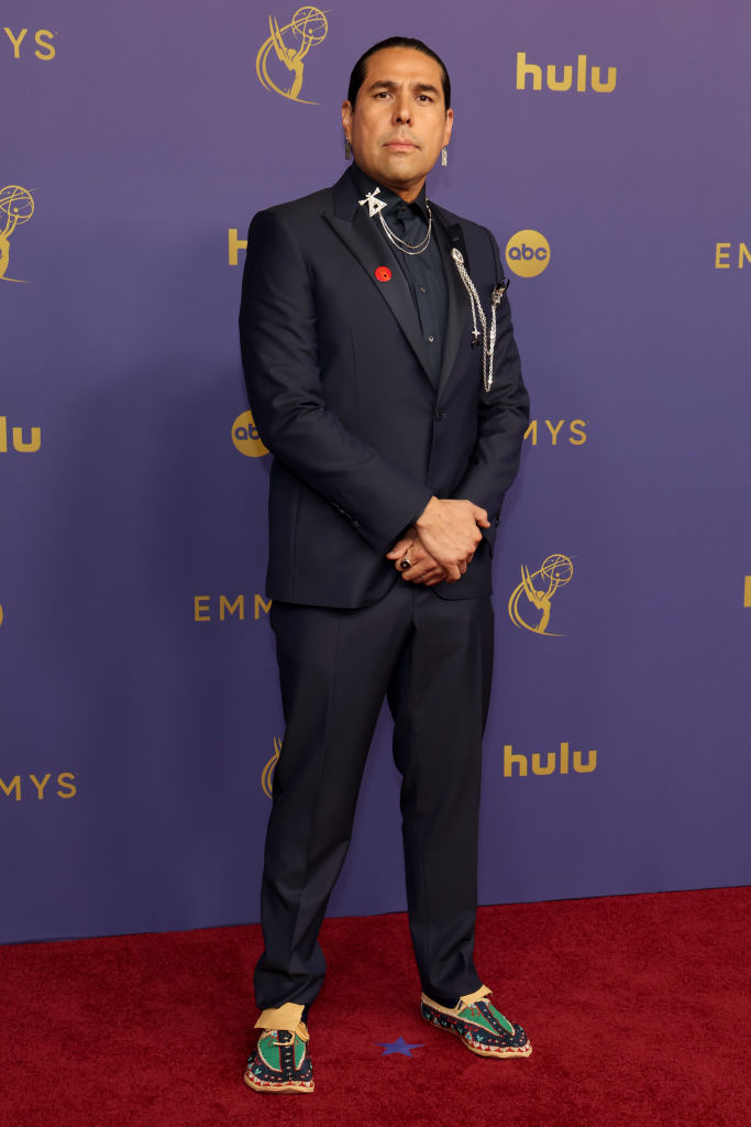 Man on the red carpet at the Emmys, in a black suit with unique accessories and colorful shoes