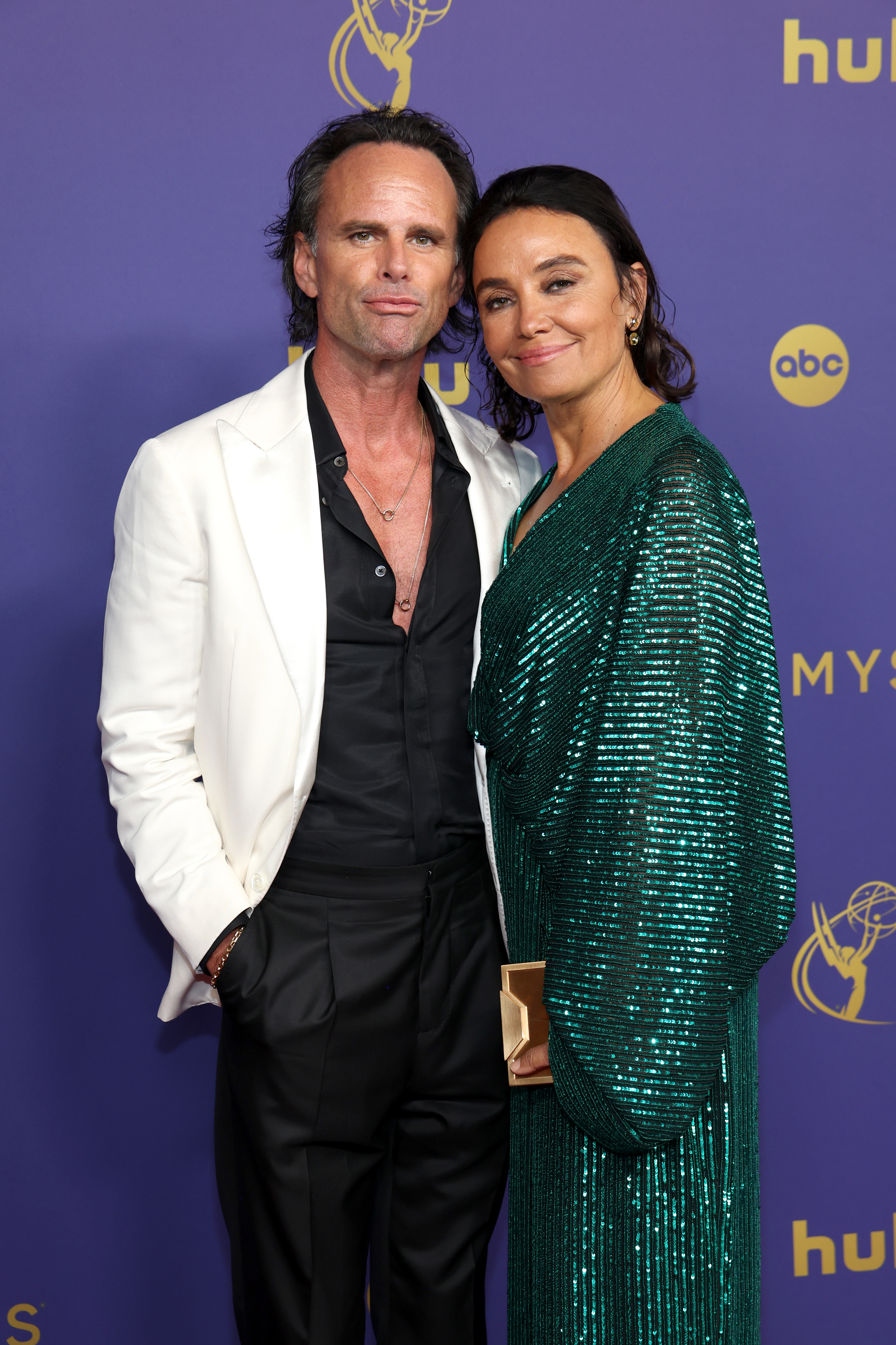 Walton Goggins in a white blazer and black shirt, and Nadia Conners in a shimmering dress, posing together at a TV event