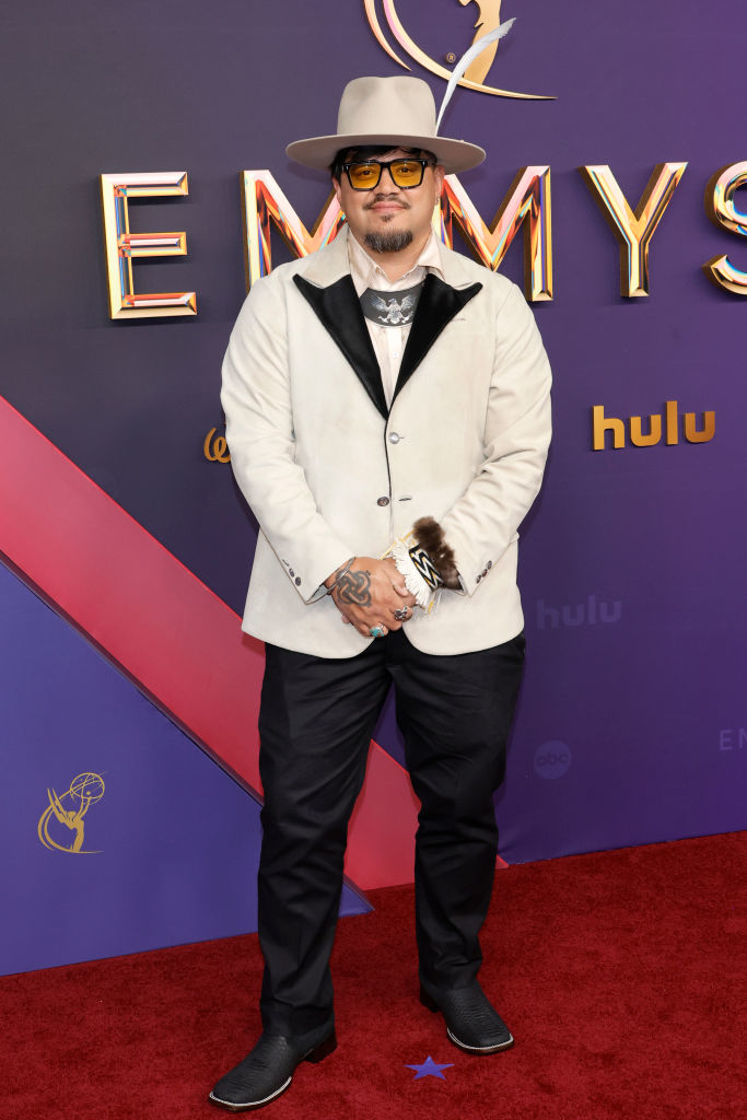 Man in a white jacket, black pants, and a beige wide-brim hat on the red carpet at the Emmys