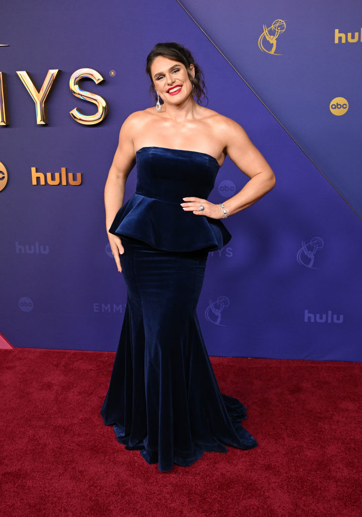 Ilona Maher poses on the red carpet wearing a strapless, form-fitting velvet gown with a peplum detail at the waist, accessorized with jewelry