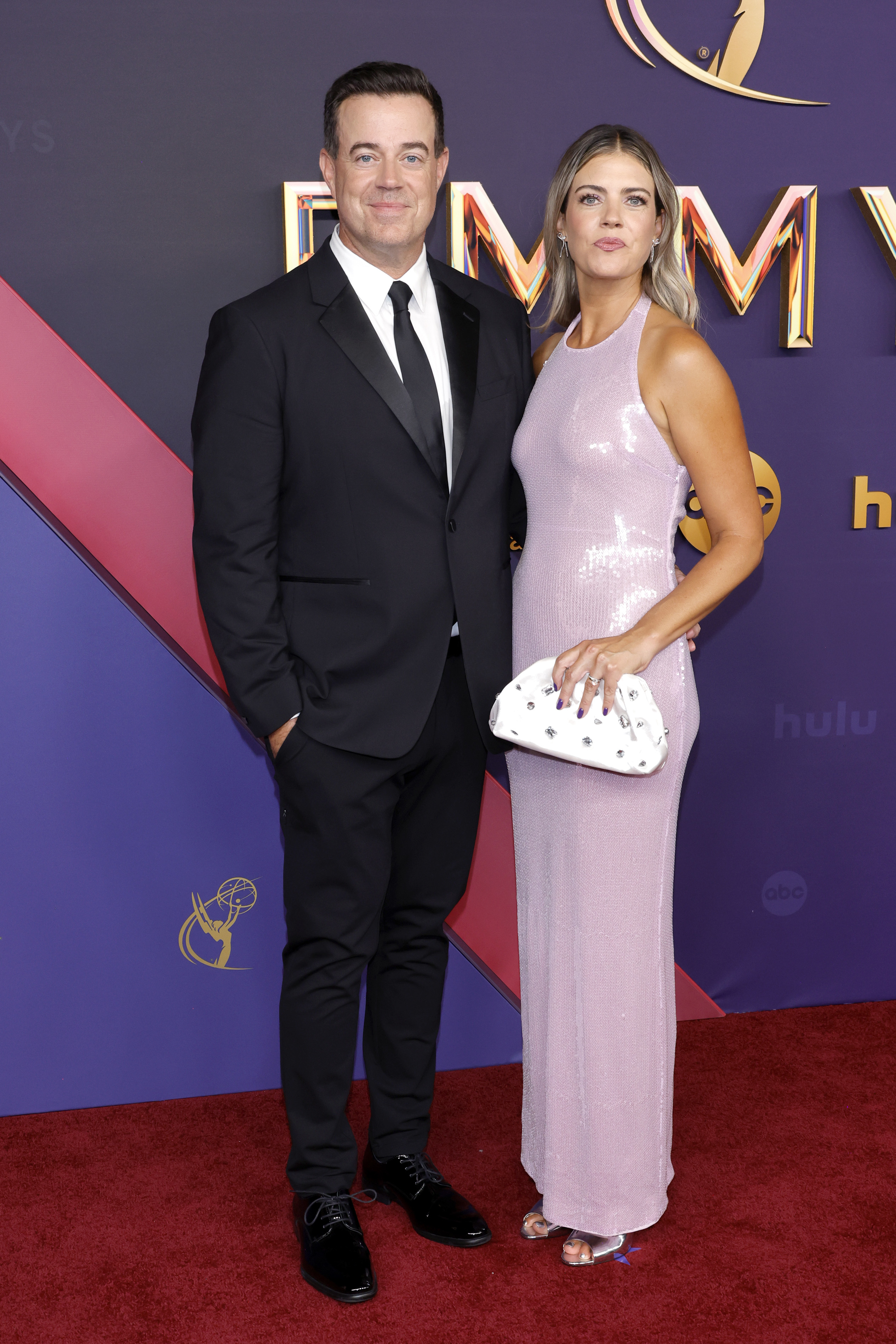 Carson Daly in a classic black suit and Siri Pinter in a sleeveless shimmering dress on the red carpet at the Emmys