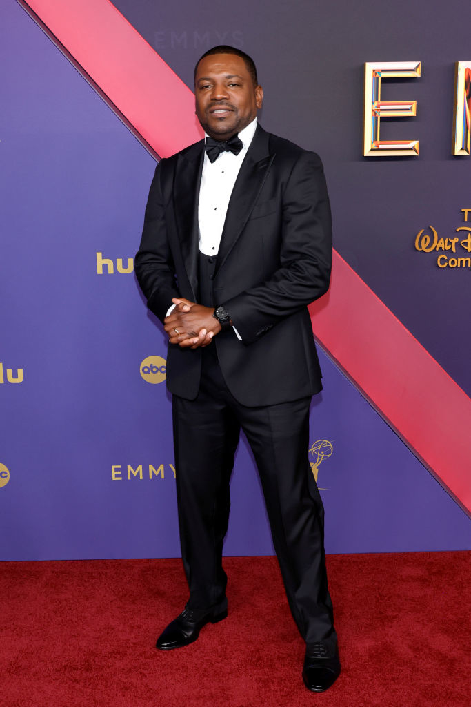 A man in a black tuxedo and bow tie poses on the red carpet at the Emmys event with a Hulu and ABC backdrop
