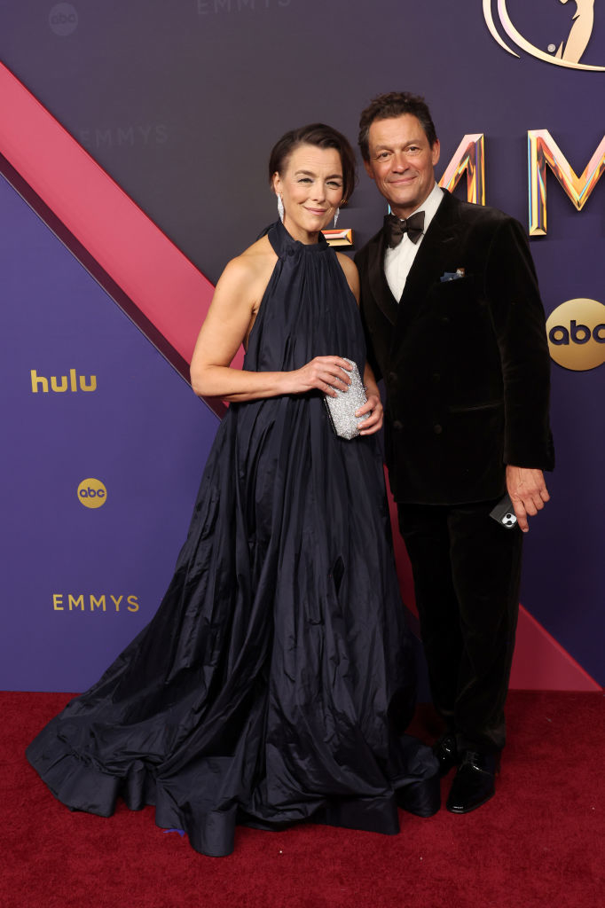Dominic West and Catherine FitzGerald pose on the red carpet at the Emmys. Catherine wears an elegant halter-neck gown, and Dominic wears a classic black tuxedo