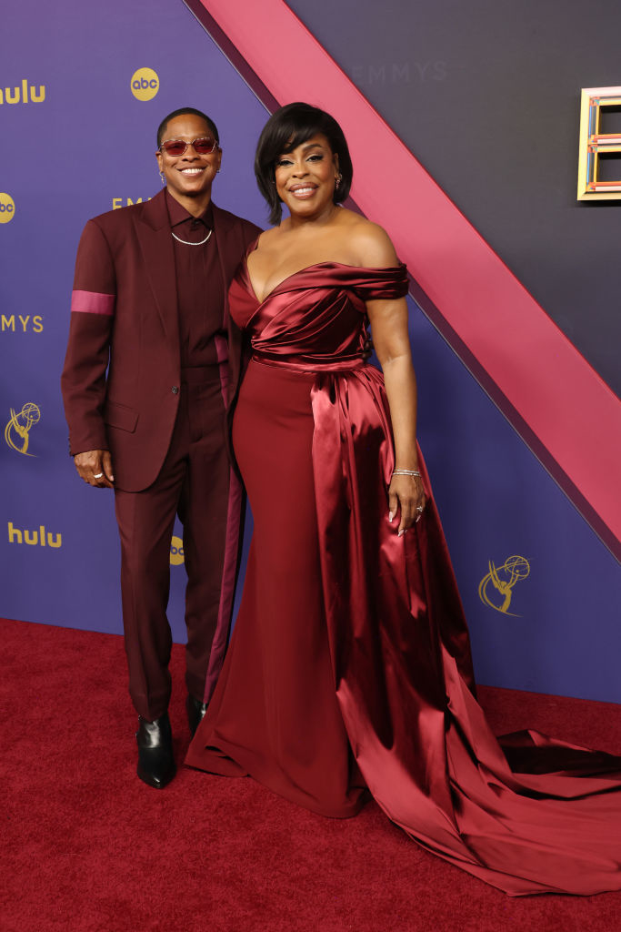 Niecy Nash-Betts and Jessica Betts pose on the red carpet. Niecy wears a strapless gown with a train, and Jessica wears a tailored suit with a matching shirt
