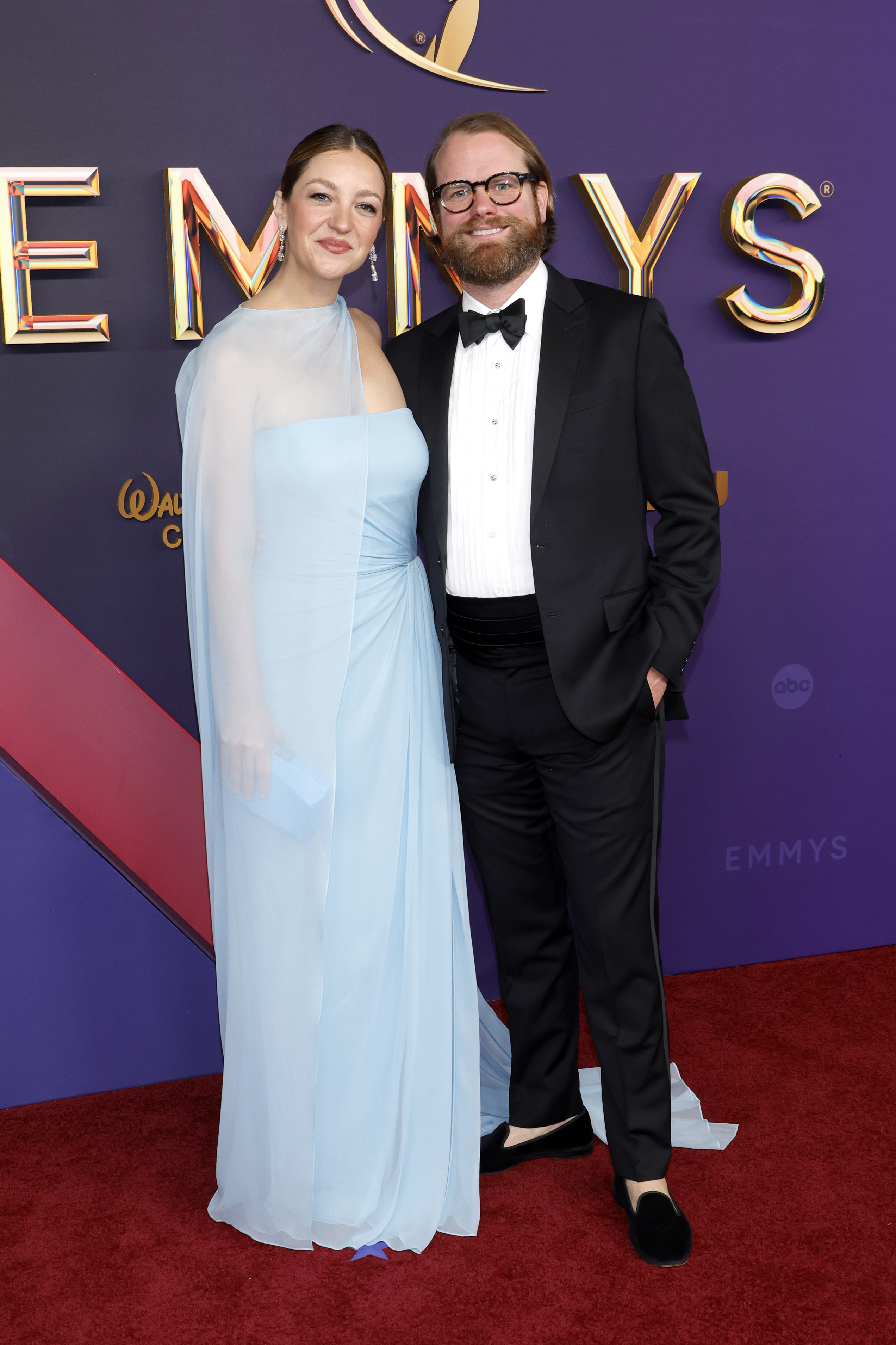 Abby Elliot in a flowing sleeveless light gown and Bill Kennedy in a tuxedo, at the Emmys red carpet event