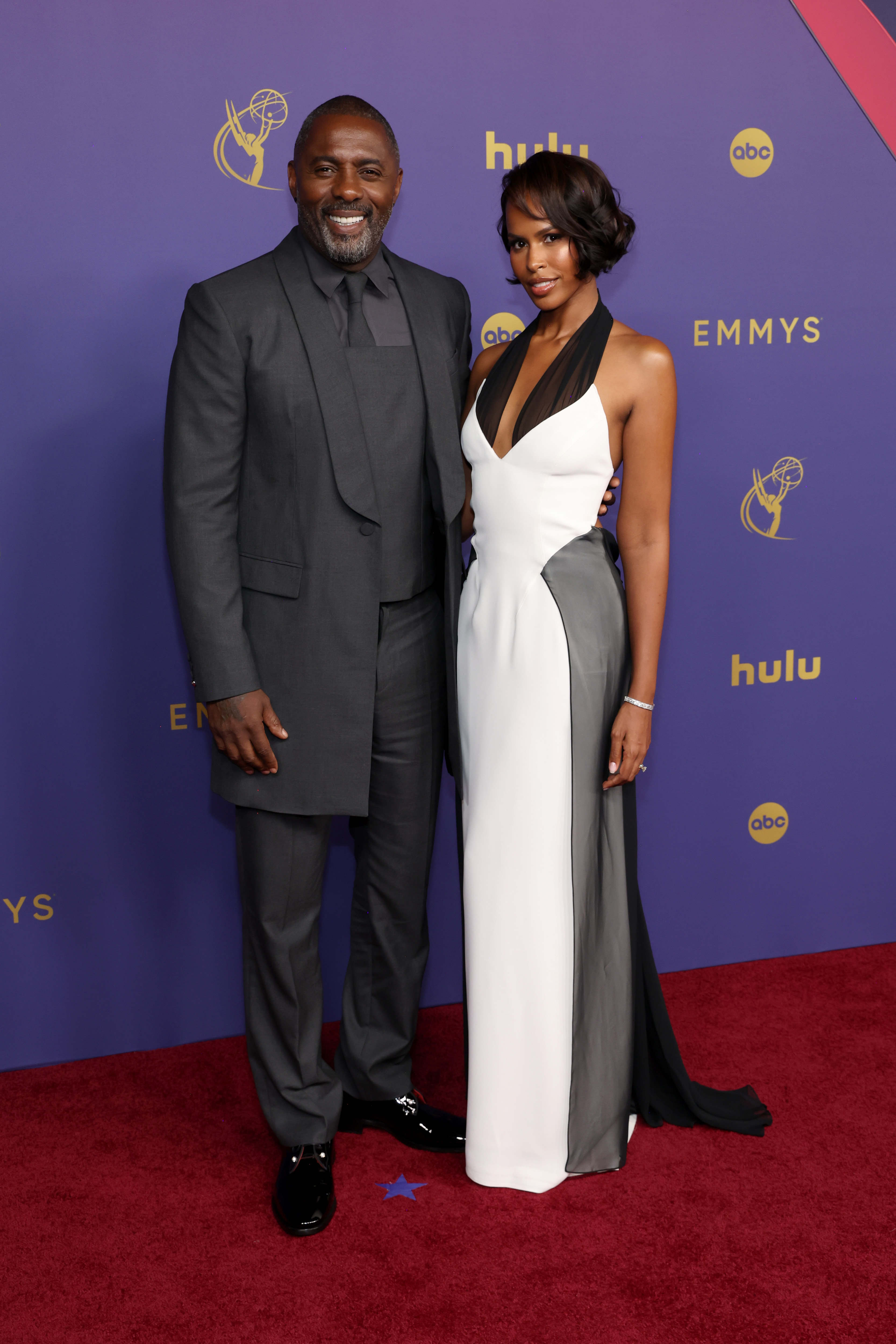 Idris Elba in a dark suit and Sabrina Dhowre Elba in a black and white gown on the Emmys red carpet