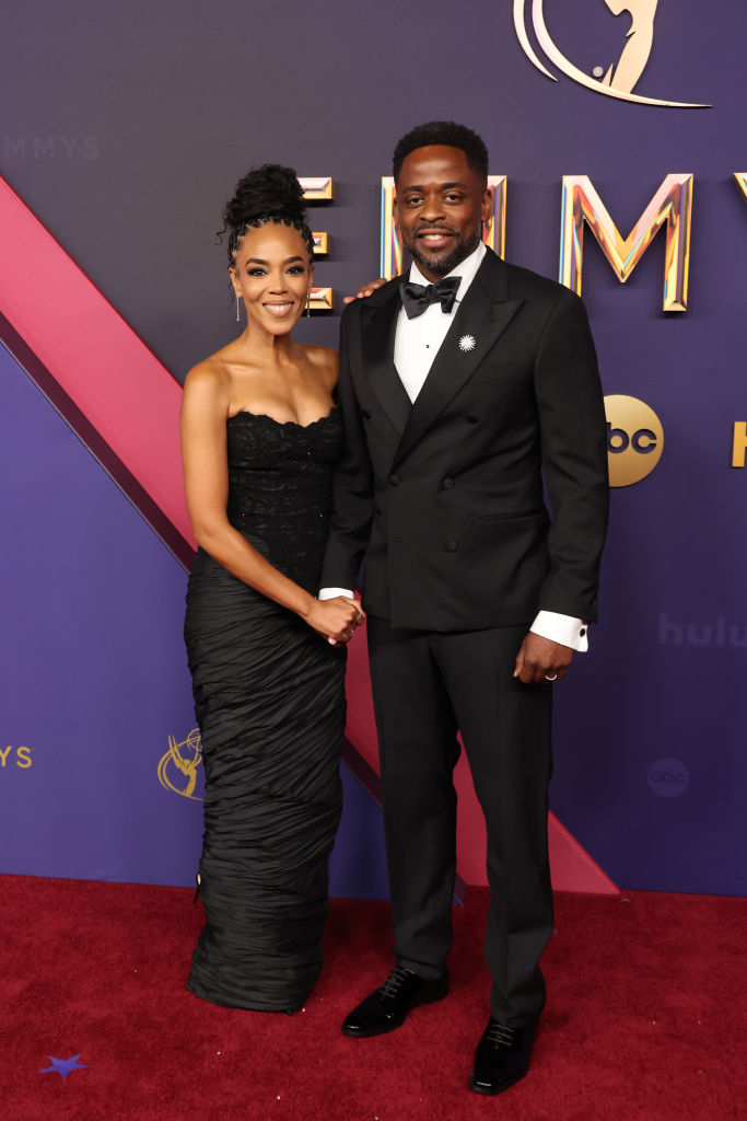 Gabrielle Dennis and Dulé Hill pose on the red carpet. Gabrielle wears a strapless black gown, and Dulé wears a black tuxedo