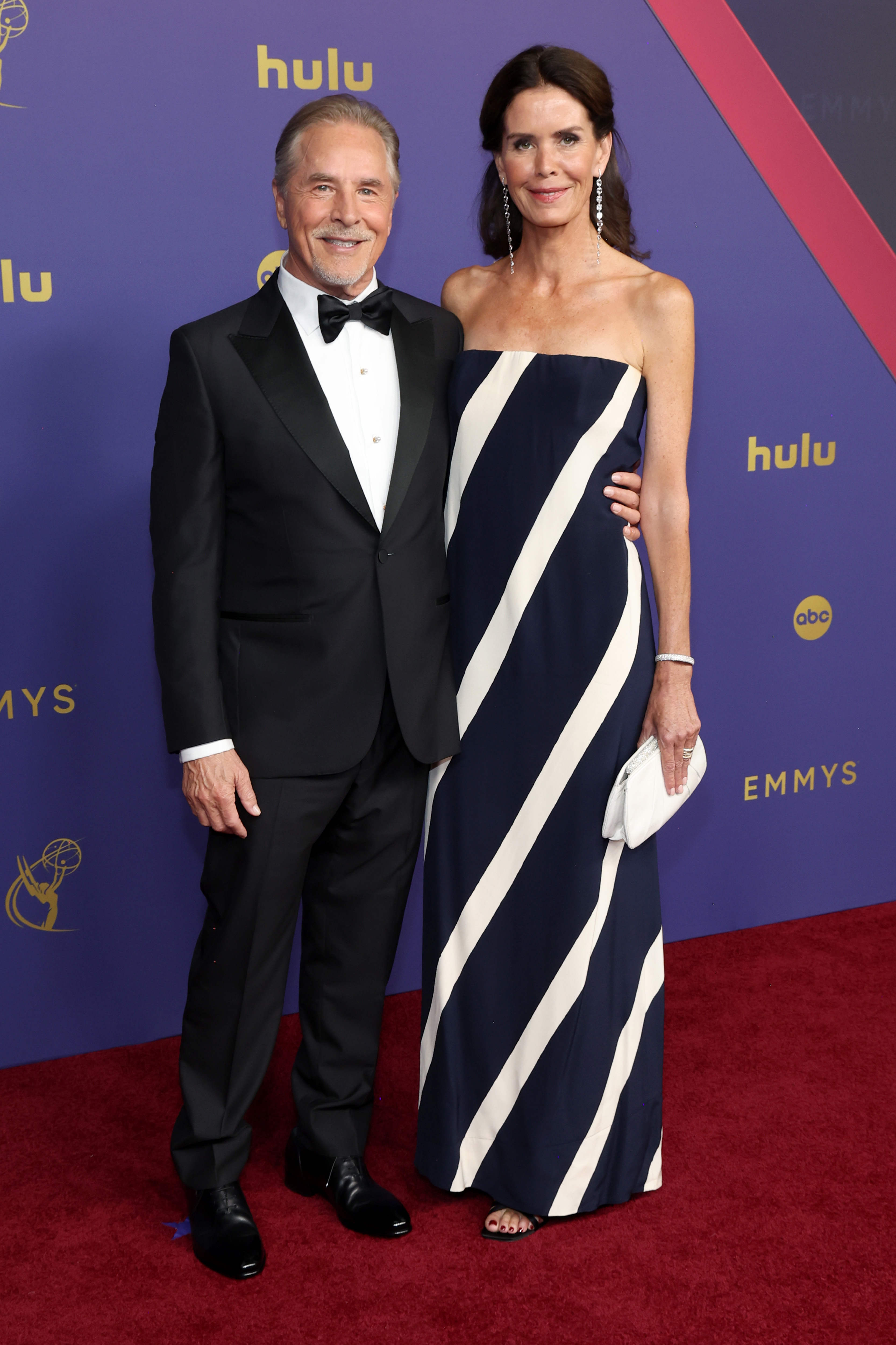 Don Johnson and Kelley Phleger on the red carpet at the Emmys. Don is in a classic black tuxedo, and Kelley is wearing a strapless gown with diagonal stripes