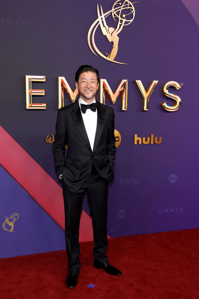 Ken Jeong on the red carpet at the Emmys, wearing a classic black tuxedo with a bow tie, standing and smiling