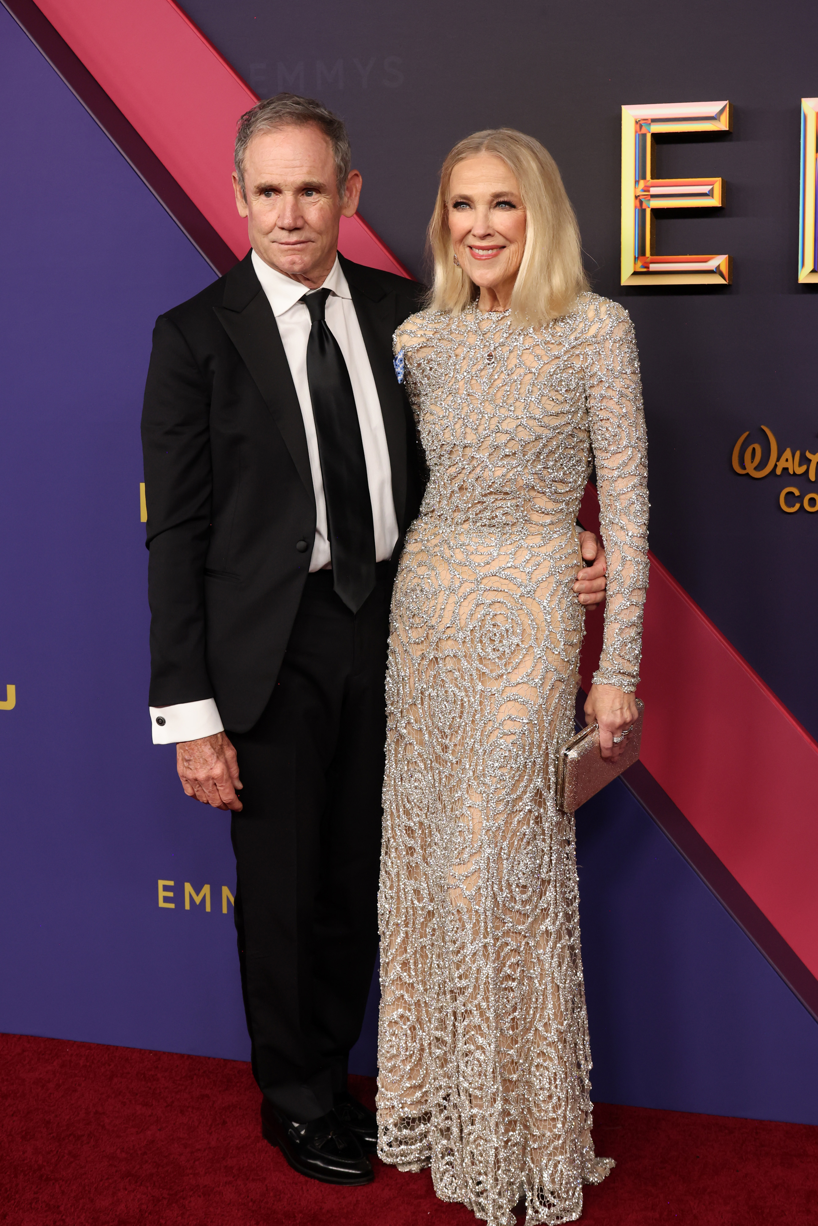 Bo Welch and Catherine O'Hara pose on the red carpet; Bo wears a black suit, and Catherine wears a beaded, floor-length gown