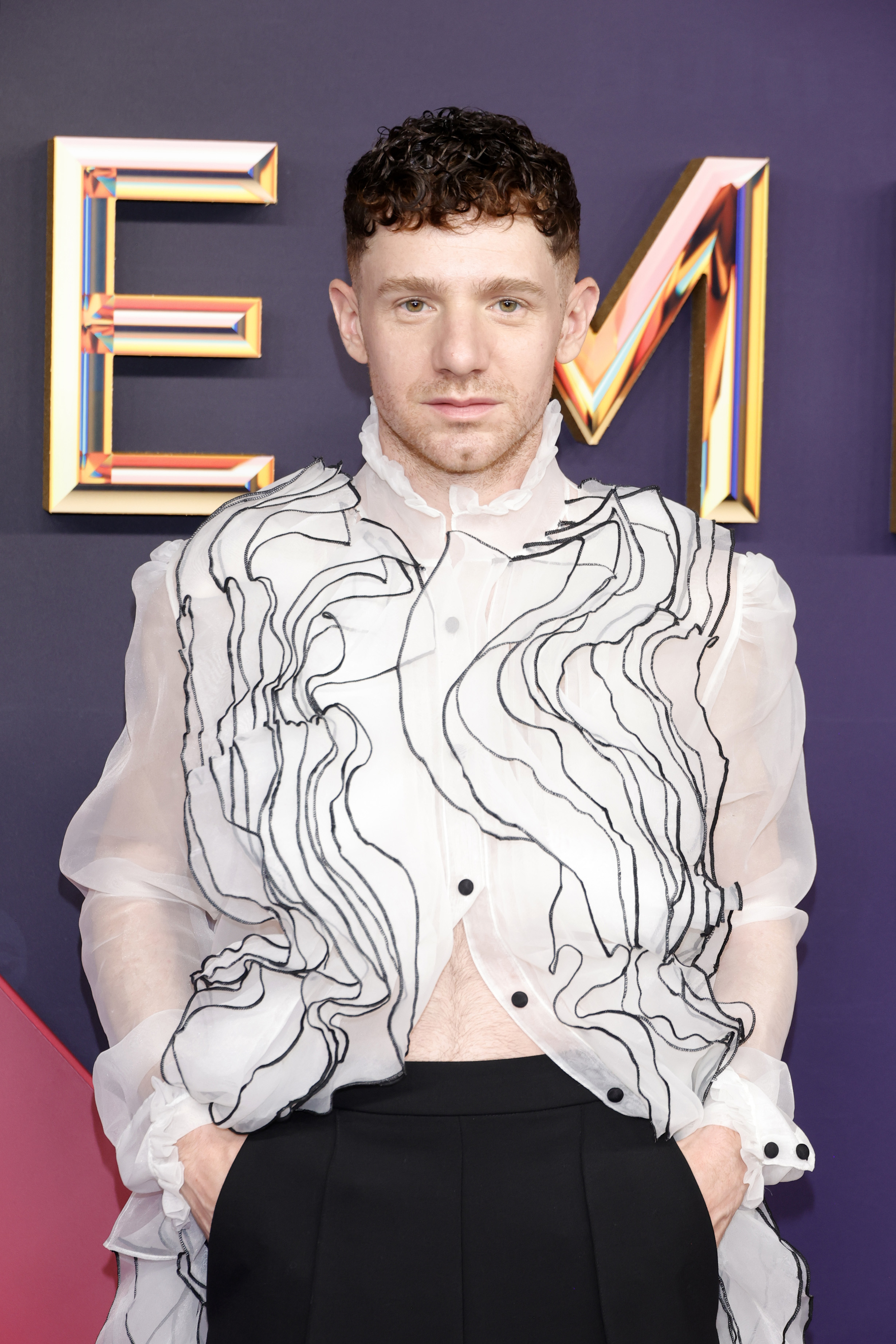 Chris Perfetti poses on the red carpet in a sheer wavy-patterned top with pants at a celebrity event