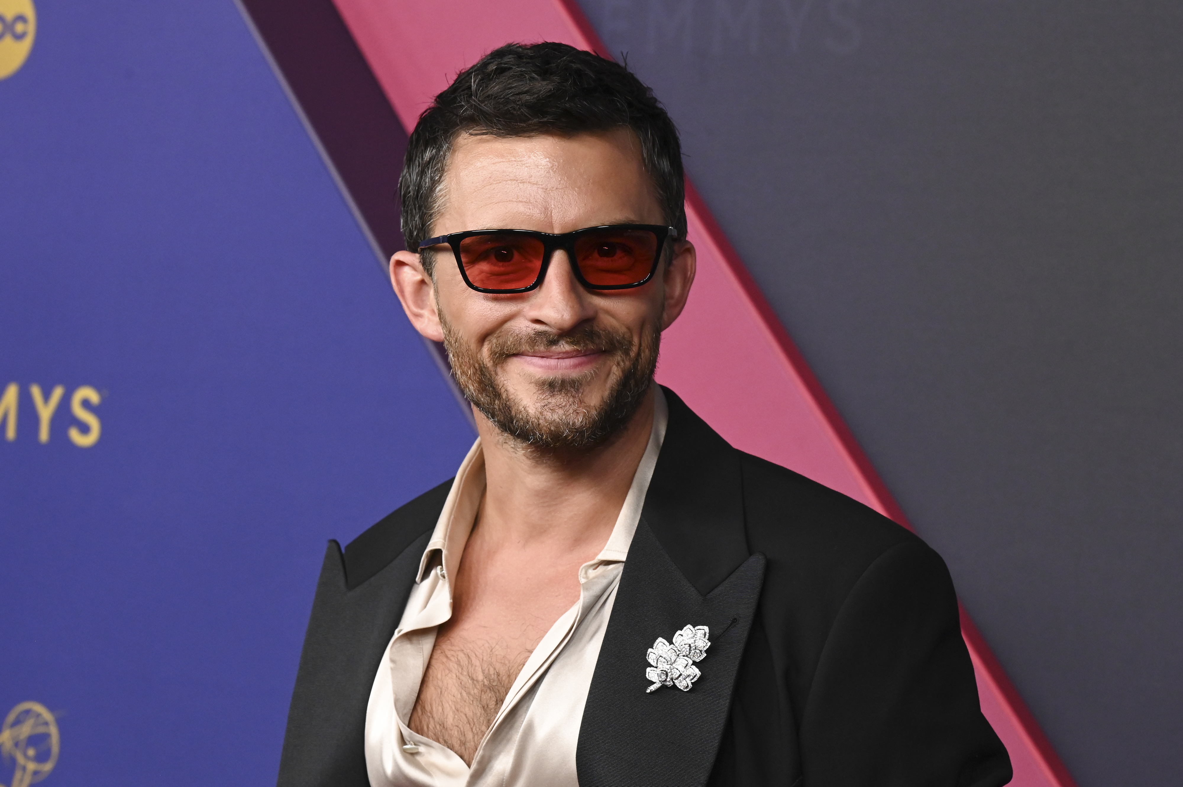 Jonathan Bailey on the red carpet in a blazer and tinted glasses