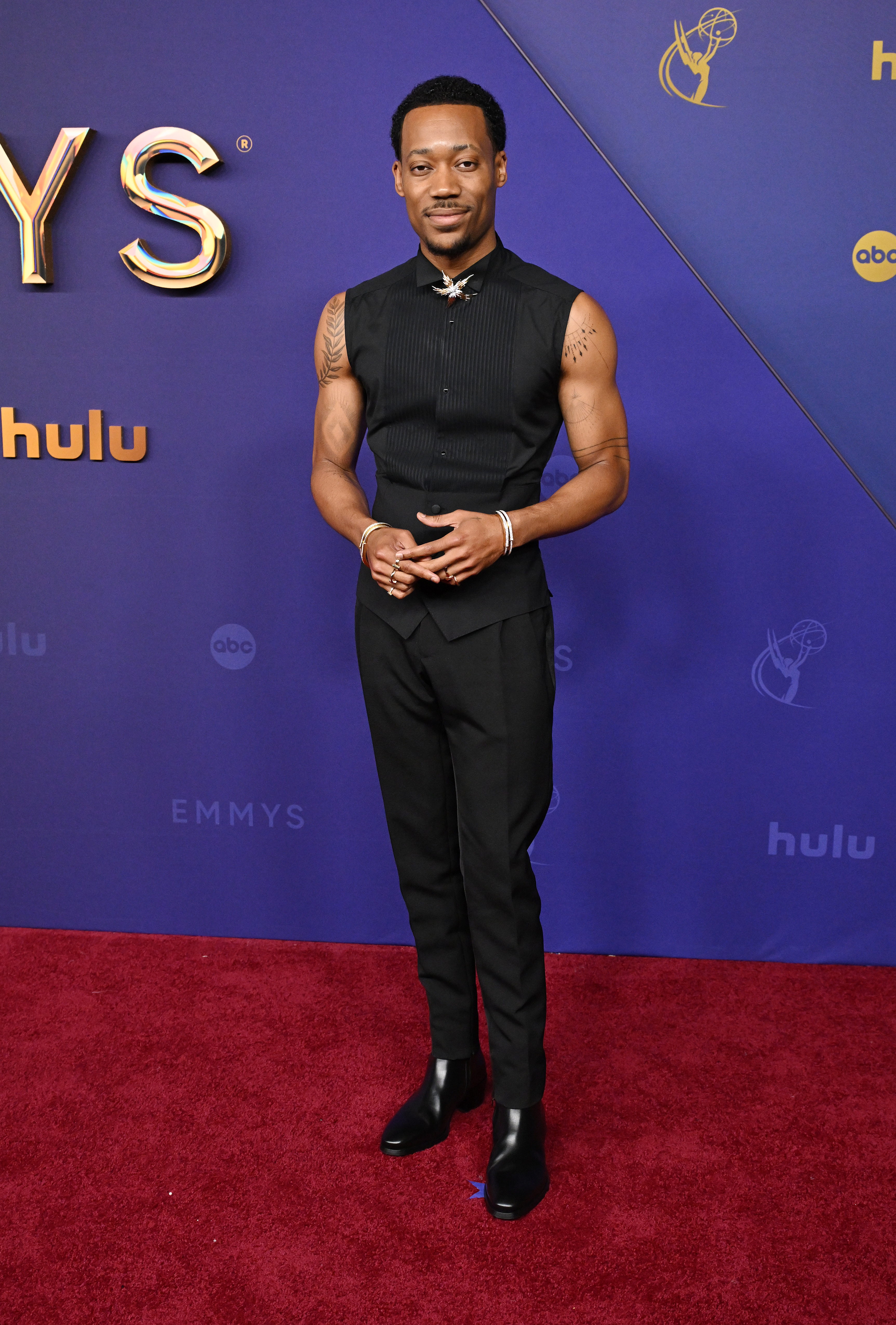 Tyler James Williams poses on the red carpet at an event, wearing a sleeveless top and pants