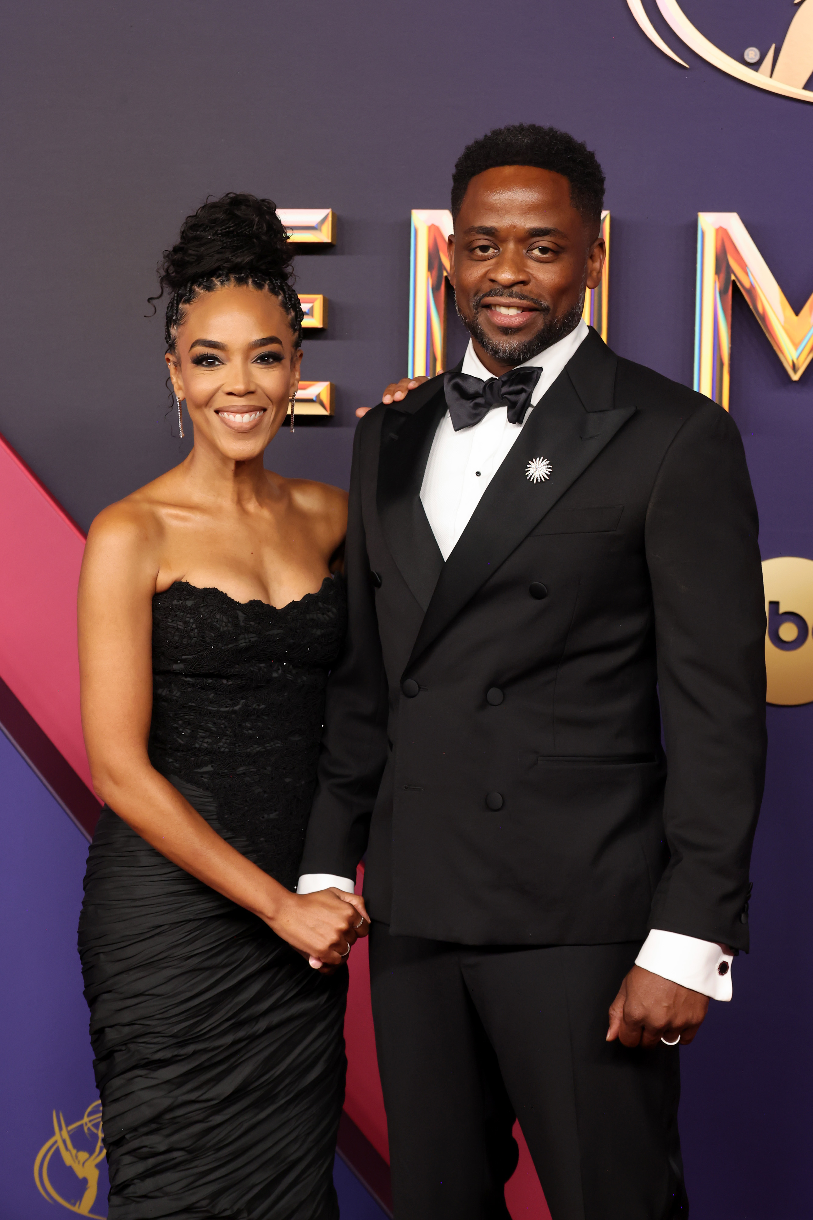 Jazmyn Simon and Dulé Hill posing on the red carpet: Jazmyn in a strapless black dress holding hands with Dulé in a double-breasted black tuxedo with a brooch