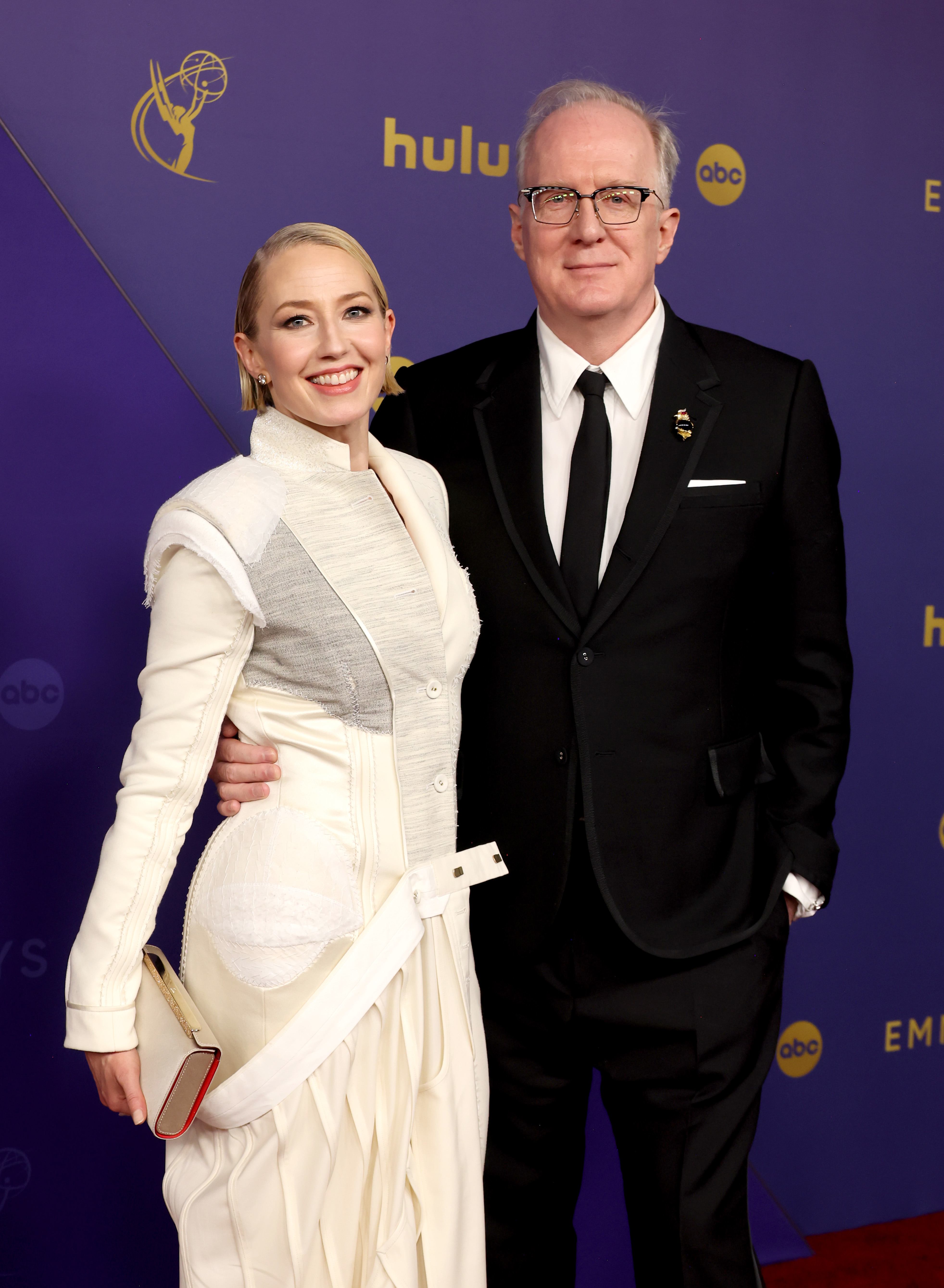 Carrie Coon and Tracy Letts at the Emmys. Carrie wears a white embellished gown, and Tracy wears a black suit with a white shirt and black tie