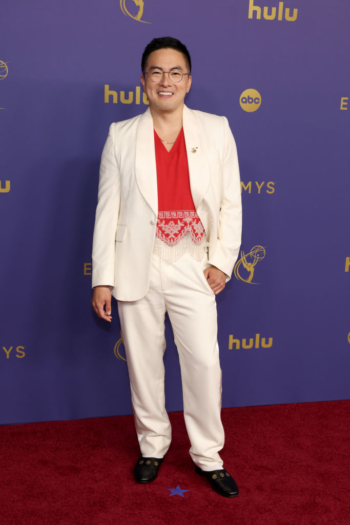 Bowen Yang on the red carpet in a white suit with a red shirt, attending the Emmys