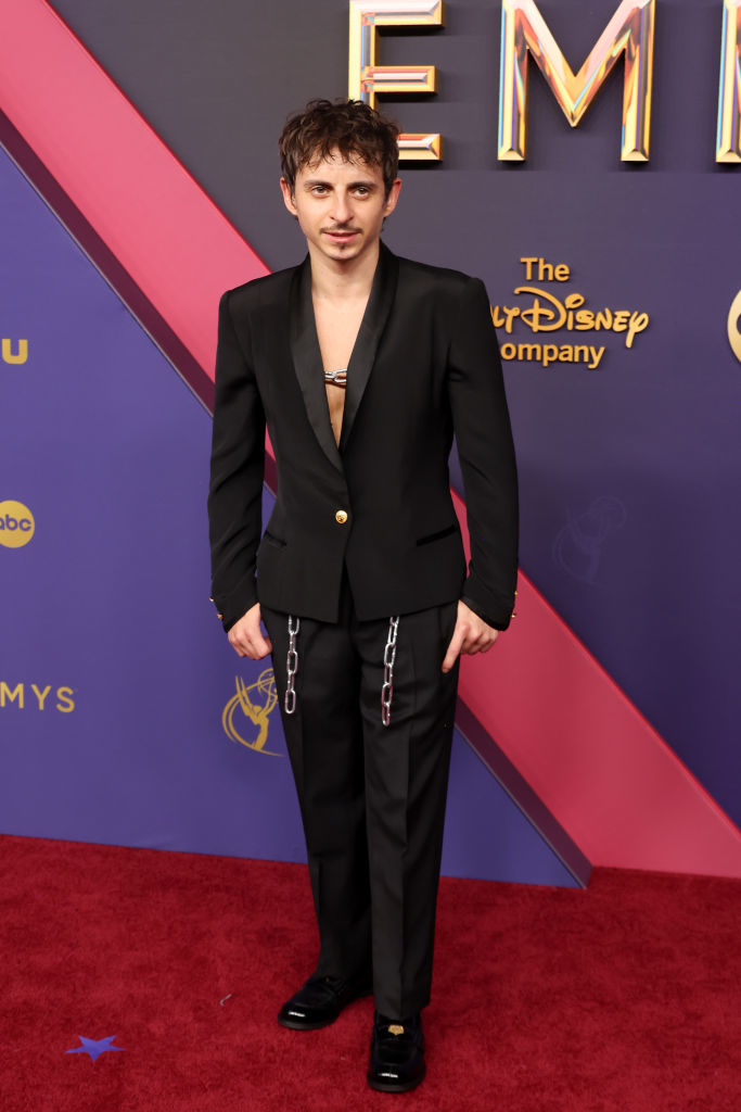 Person wearing a black suit and loafers, with a chain detail on the pants, standing on the red carpet at an event