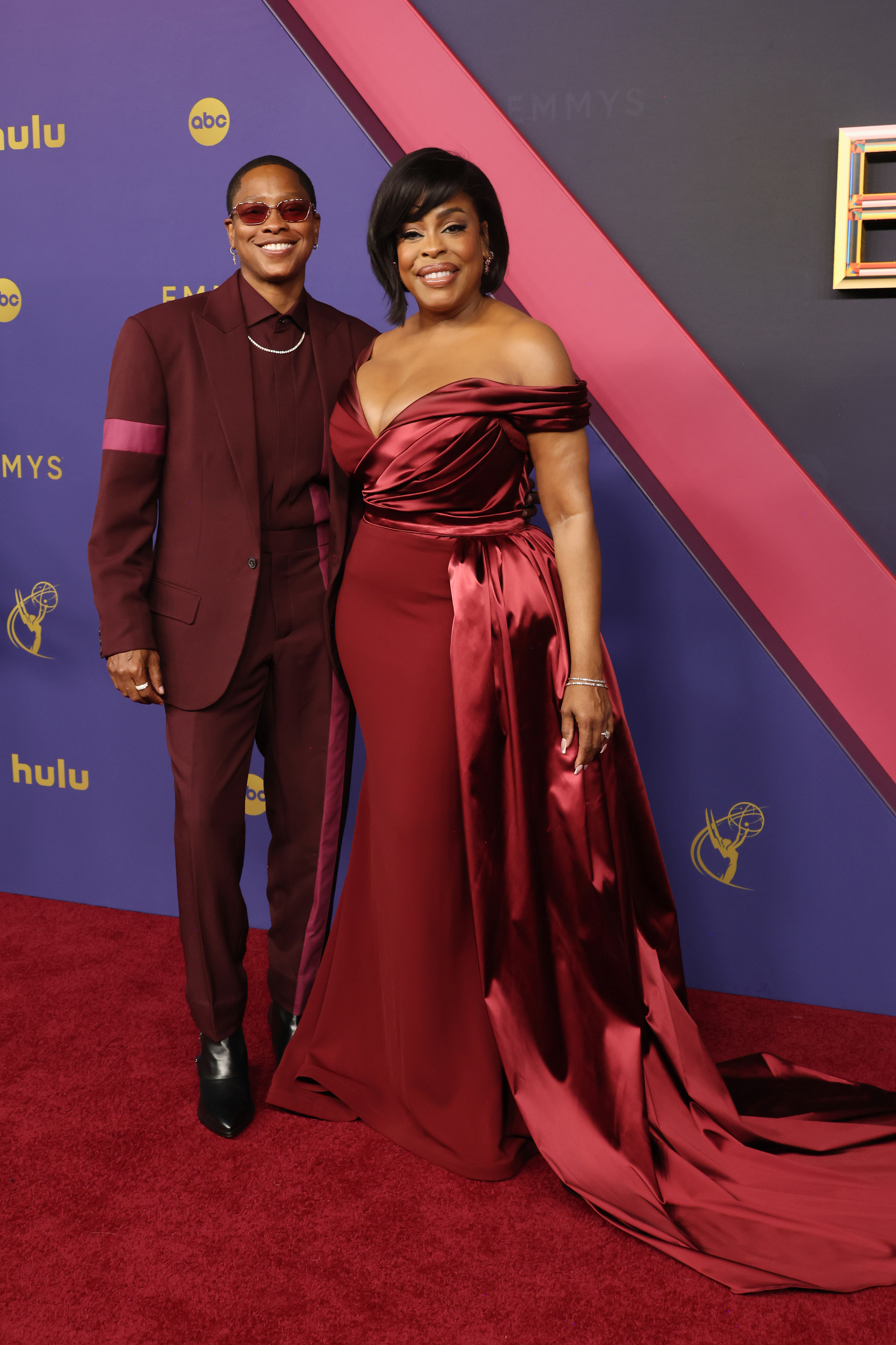 Niecy Nash and Jessica Betts at the Emmys. Niecy wears an elegant, off-shoulder gown with a train, while Jessica wears a matching suit with a turtleneck