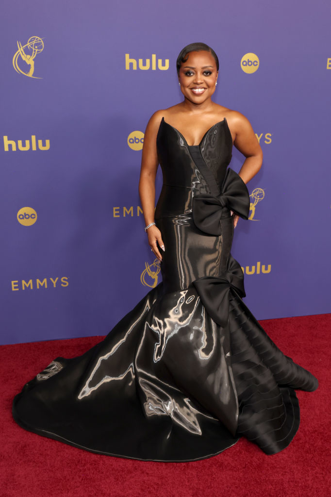 Quinta Brunson poses on a red carpet in an elegant, form-fitting gown with large bow accents at the 2022 Emmys