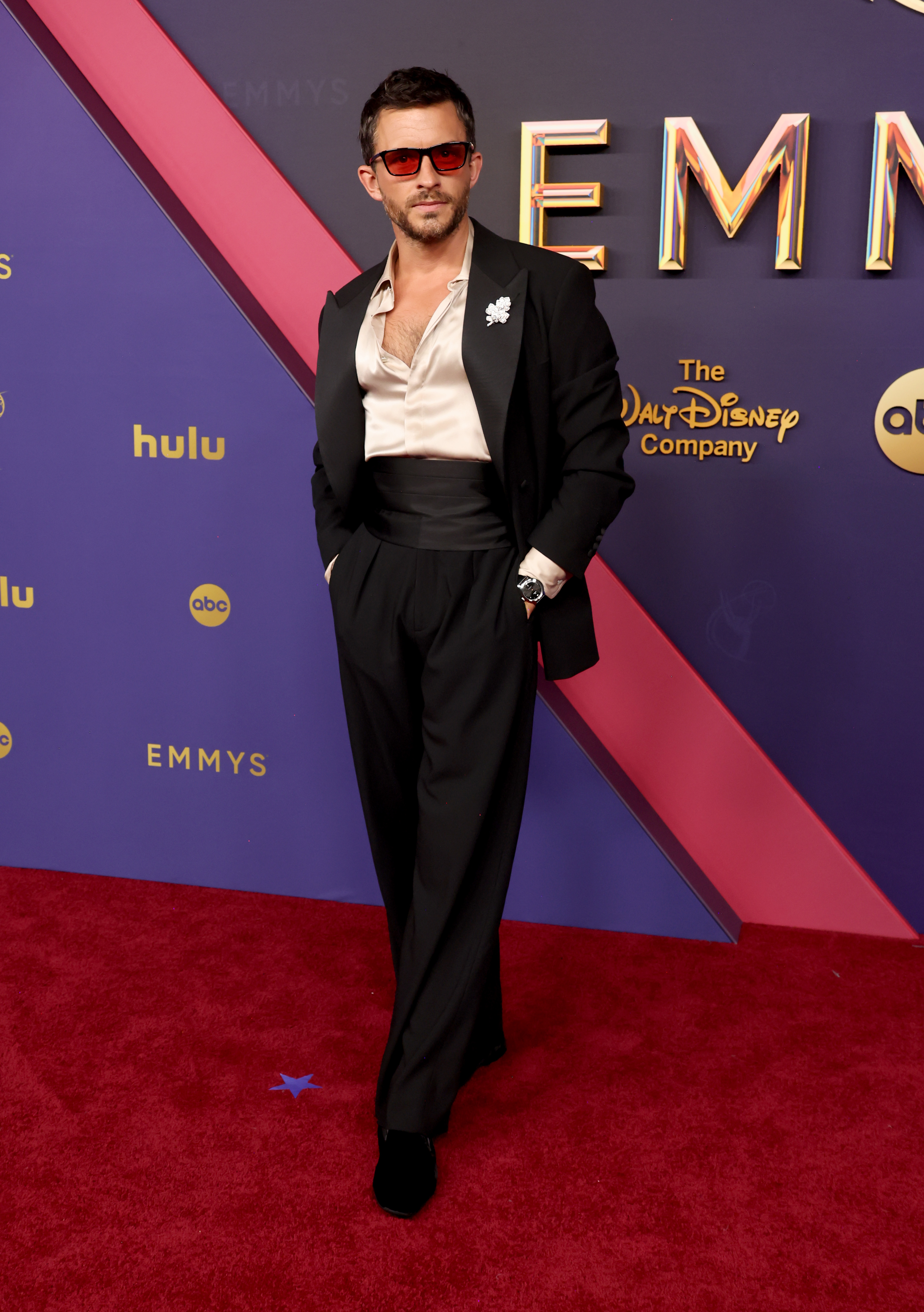 Jonathan Bailey in formal attire with sunglasses, posing on a red carpet at the Emmys