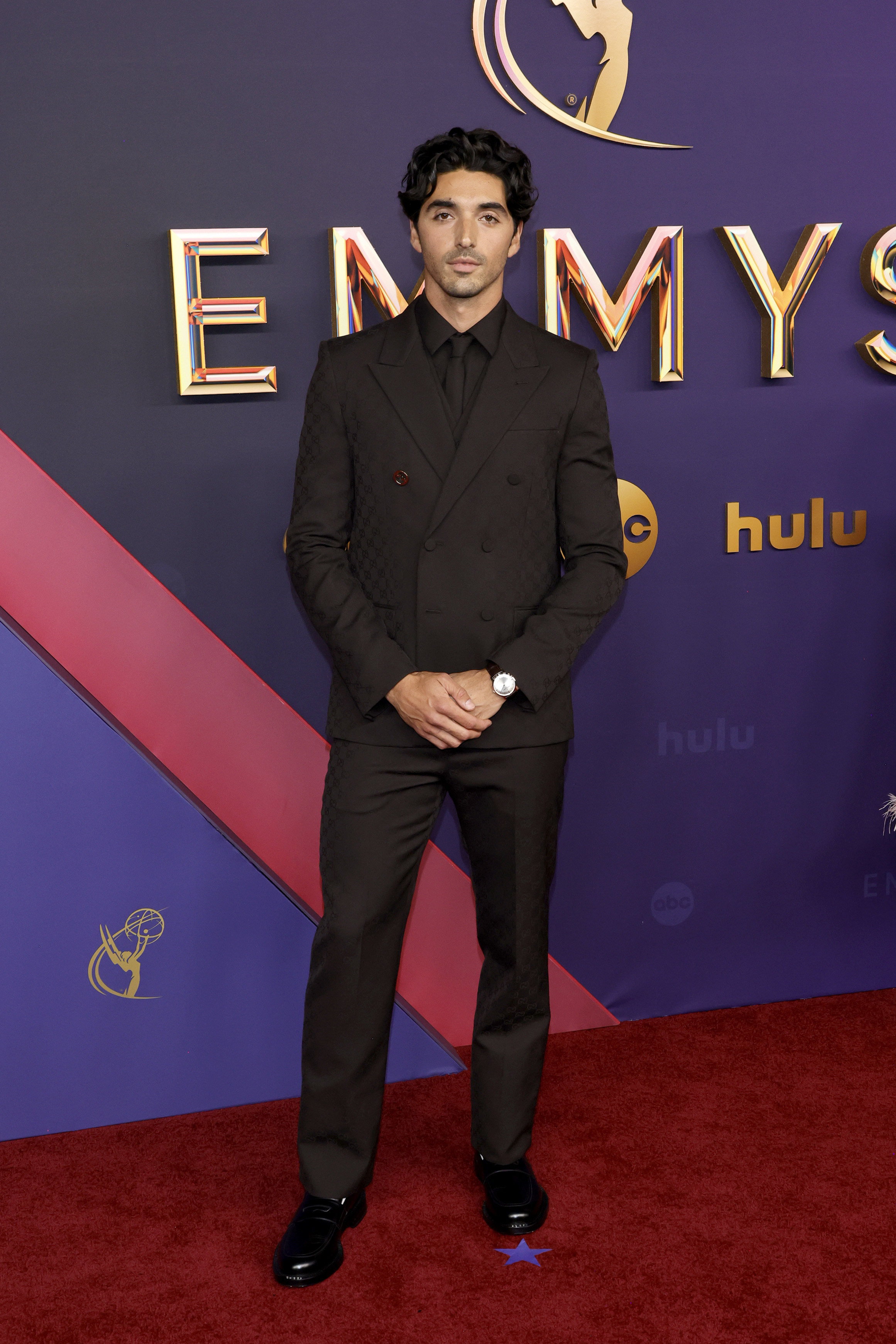 Taylor Zakhar Perez in a suit with a patterned jacket stands on a red carpet at the Emmys