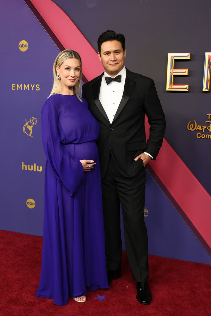 Ali Fedotowsky and Nick Lee at an Emmy Awards event. Ali is wearing a flowing gown, and Nick is in a classic tuxedo. Both are smiling at the camera