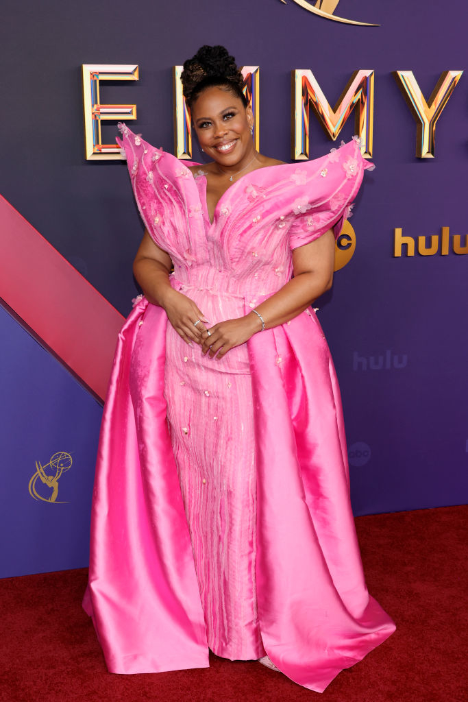 Quinta Brunson at the Emmys, standing on the red carpet in a gown with dramatic shoulder details