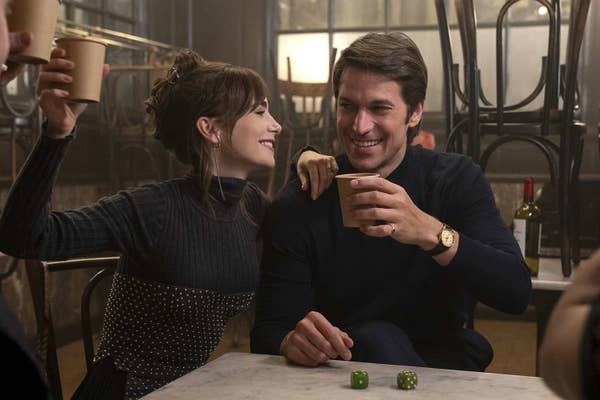 Lily Collins and Lucas Bravo in a scene from a TV show, smiling and toasting with cups in a cozy café setting