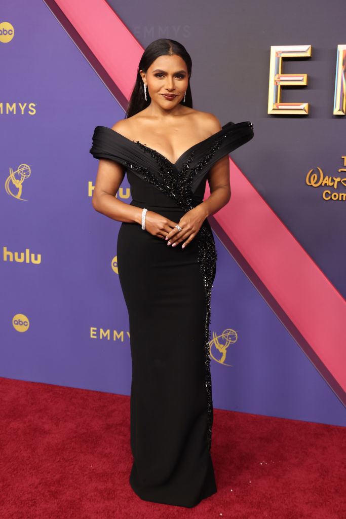 Mindy Kaling on the red carpet at the Emmys, wearing an elegant off-the-shoulder black gown with sparkling embellishments