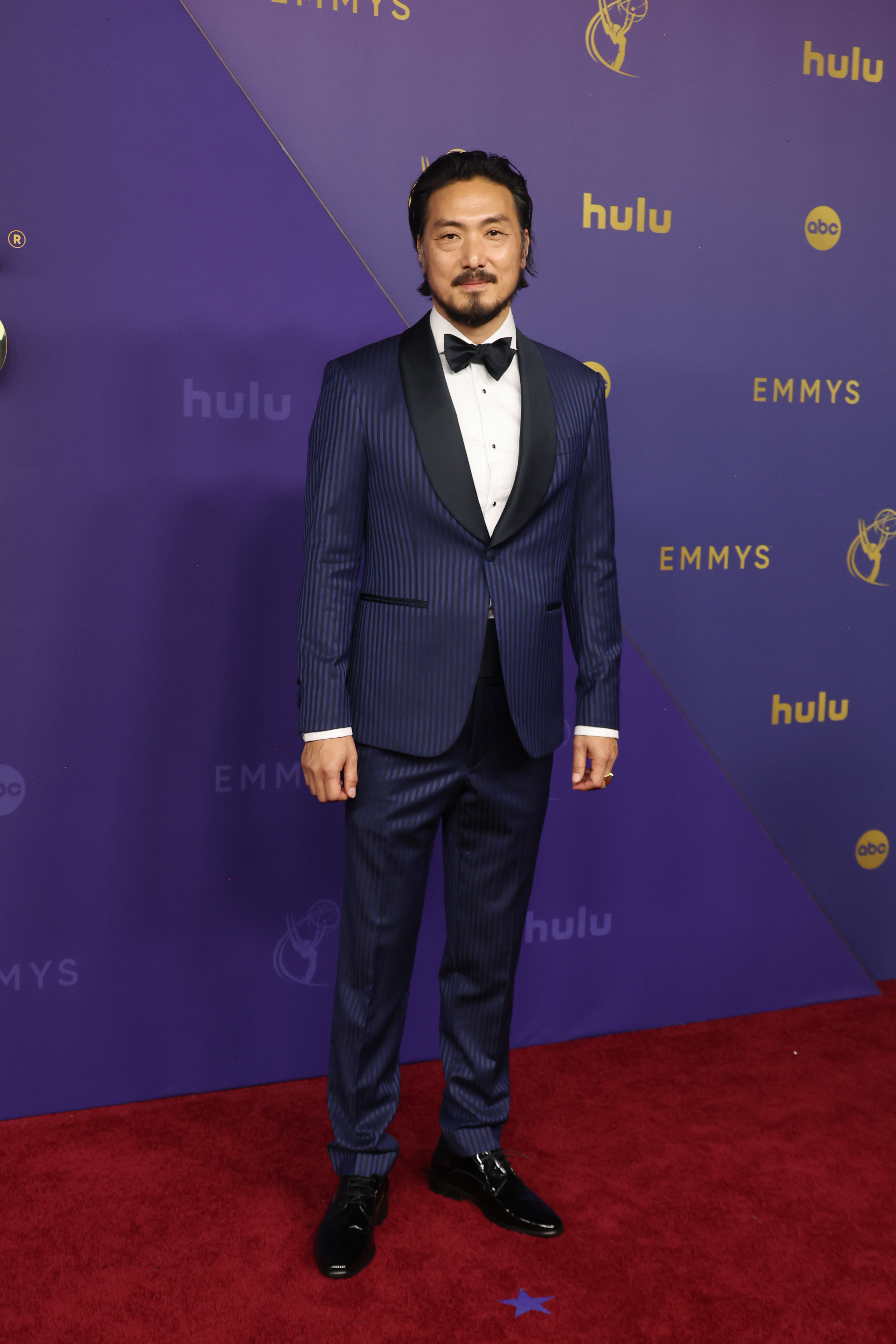 Takehiro Hira in a dark suit with a bow tie poses on the red carpet at the Emmys
