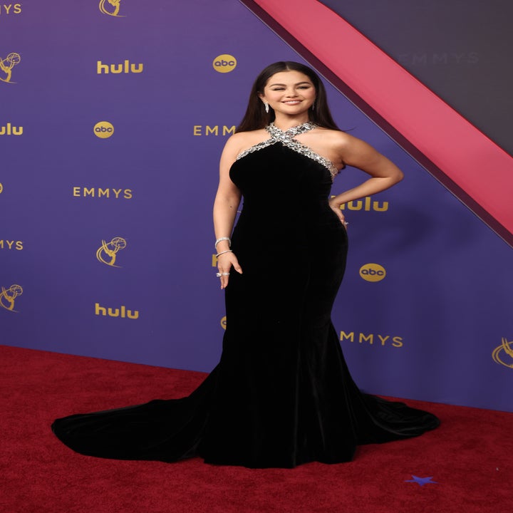 Selena Gomez poses on the red carpet at the Emmys, wearing a black, floor-length, sleeveless gown with silver embellishments around the neckline