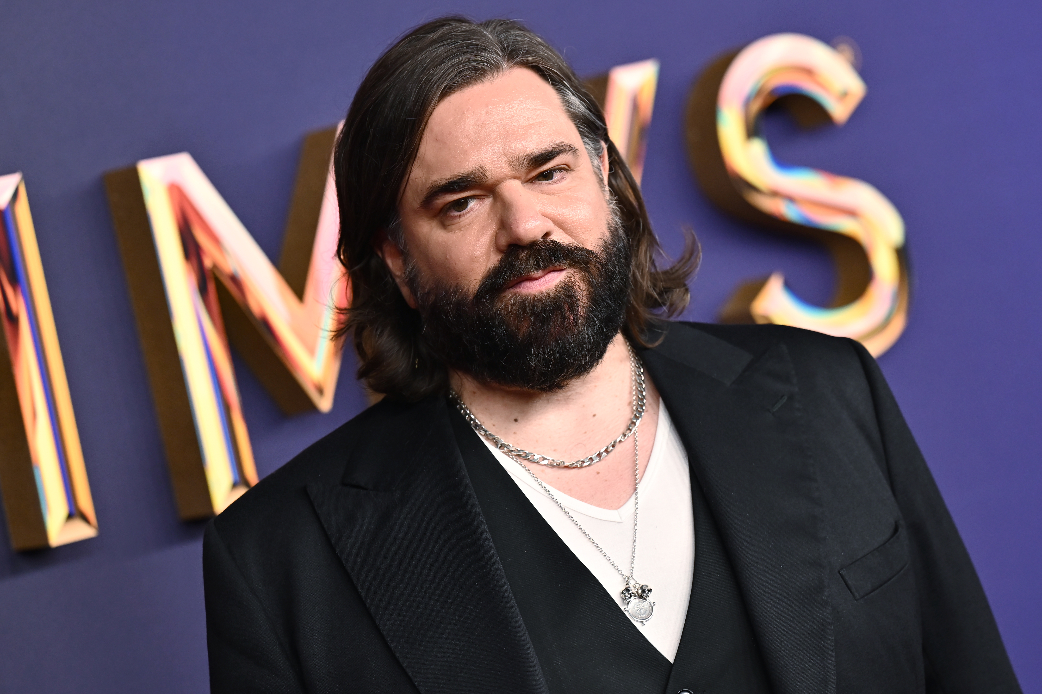 Matt Berry on the red carpet wearing a suit with a undershirt and layered necklaces