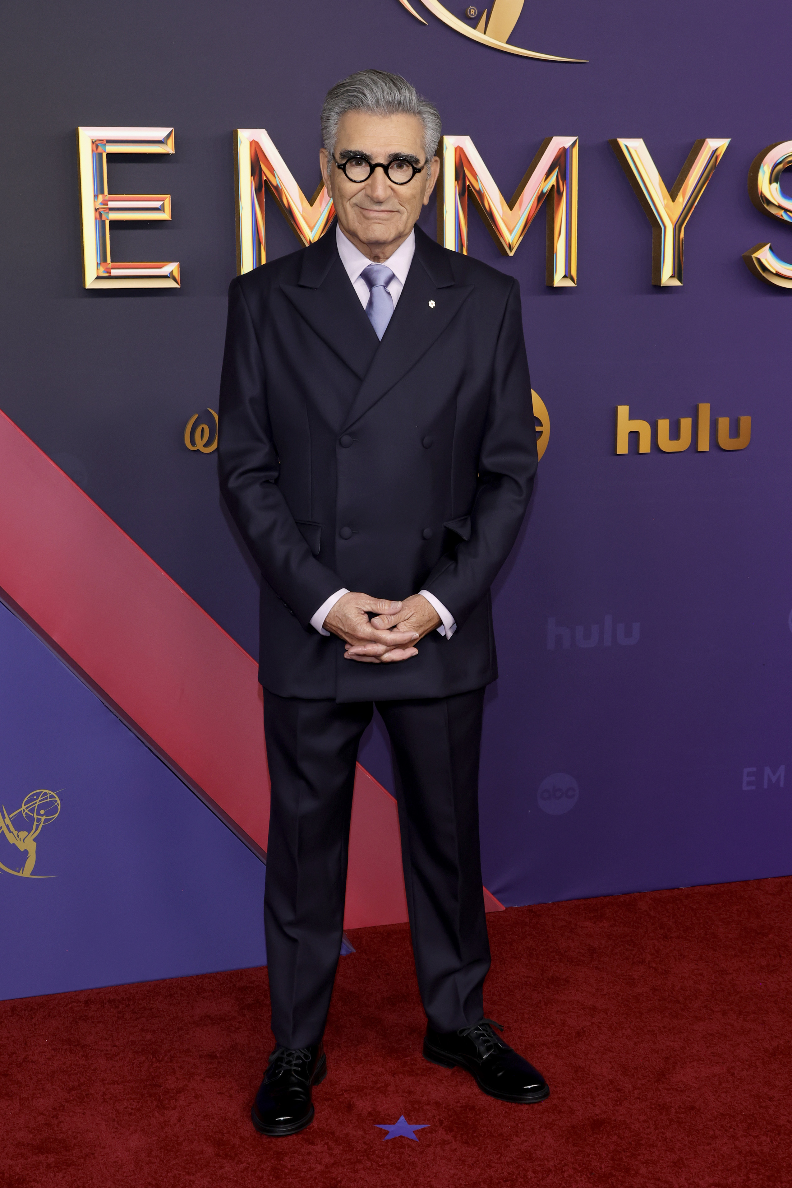Eugene Levy on the red carpet at the Emmys, wearing a dark double-breasted suit with a shirt and tie